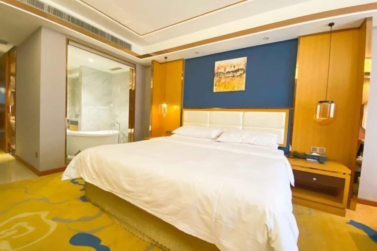 A hotel room with a large bed, a bathroom with a glass shower enclosure, and a wooden nightstand with a lamp.
