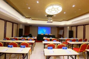 A conference room with rows of tables and chairs, a projection screen, and a podium. - Huandu Around Capital Hotel (Shantou)