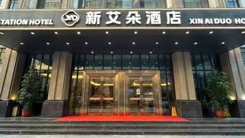 A hotel entrance with a red carpet, glass doors, and a sign above in a foreign language.