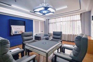 A conference room with a table, chairs, a ceiling light, a window with curtains, and a blue wall. - Huandu Around Capital Hotel (Shantou)