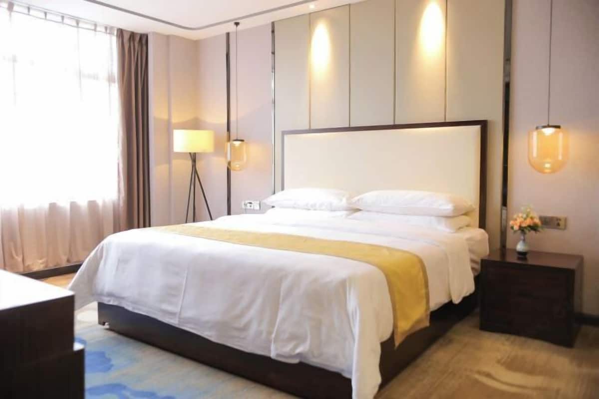 Une chambre d’hôtel avec un grand lit, une table de chevet, une lampe et une vue sur l’extérieur.