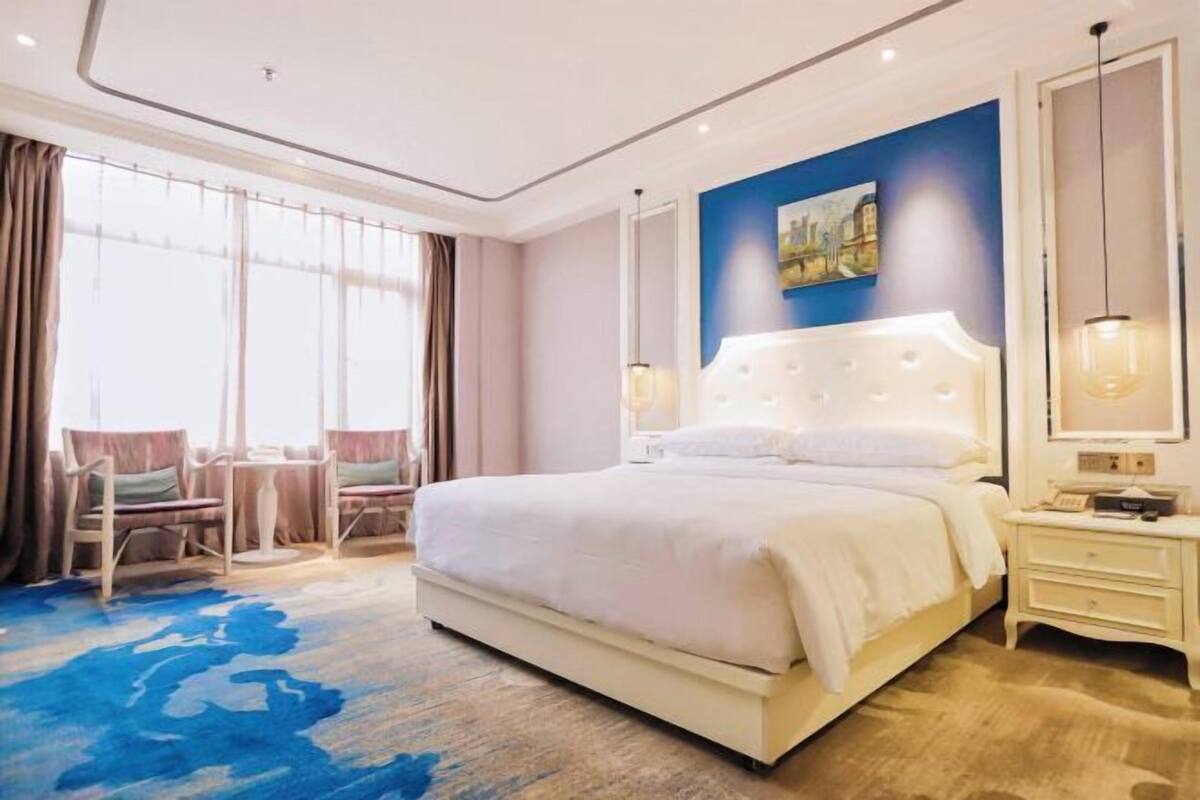 Une chambre d’hôtel moderne avec un grand lit, un coin salon avec des fauteuils et un tableau au mur.