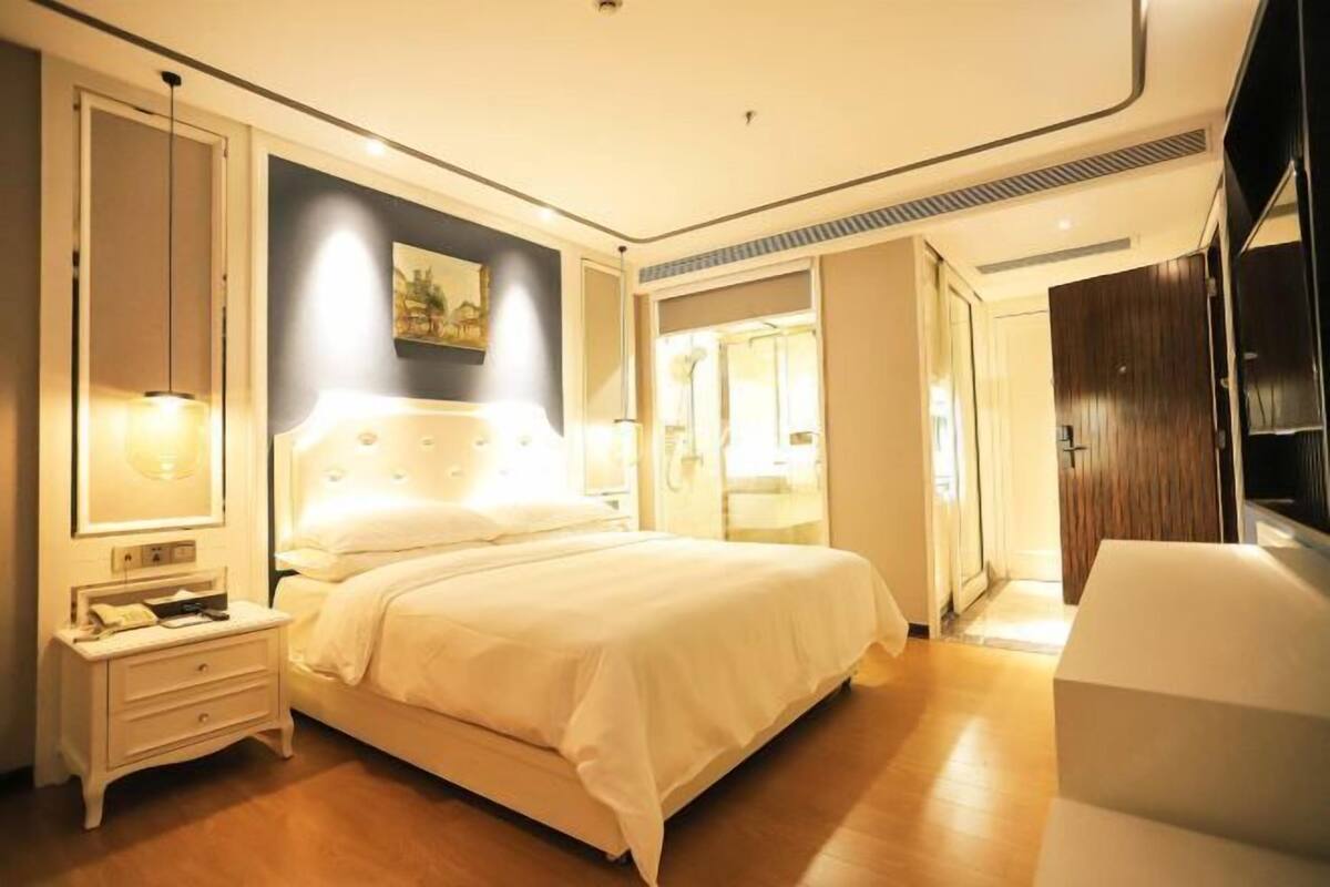 Une chambre d’hôtel moderne avec un grand lit, des tables de chevet, une petite table et un tableau au mur.