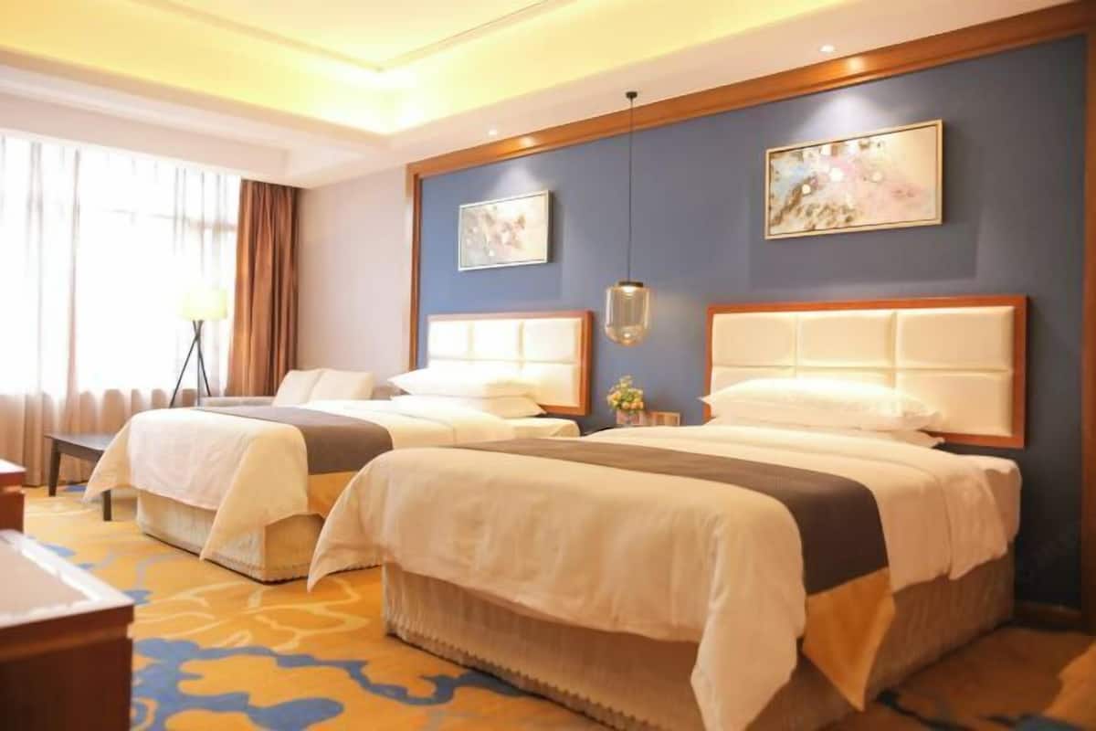 Une chambre d’hôtel avec deux lits, une grande fenêtre avec des rideaux, un lampadaire et des œuvres d’art accrochées aux murs.