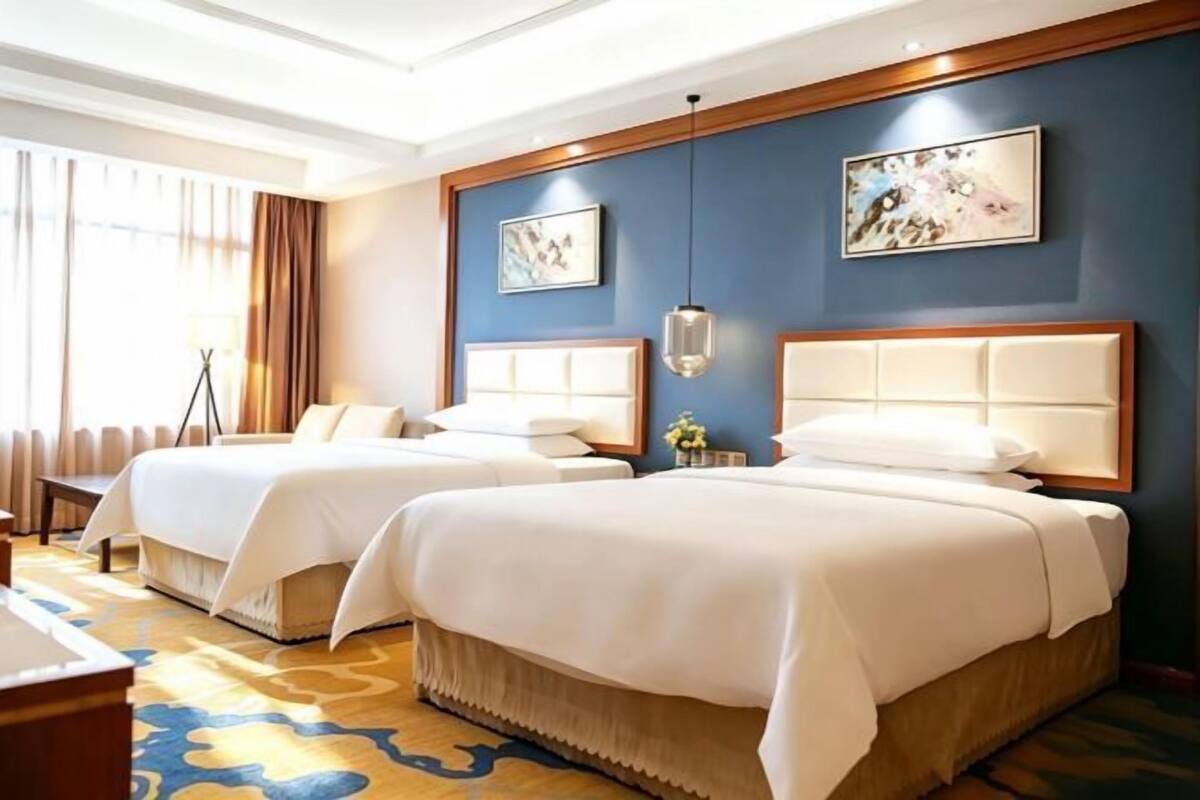 Une chambre d’hôtel avec deux lits, une grande fenêtre avec des rideaux, un lampadaire et des œuvres d’art accrochées au mur.