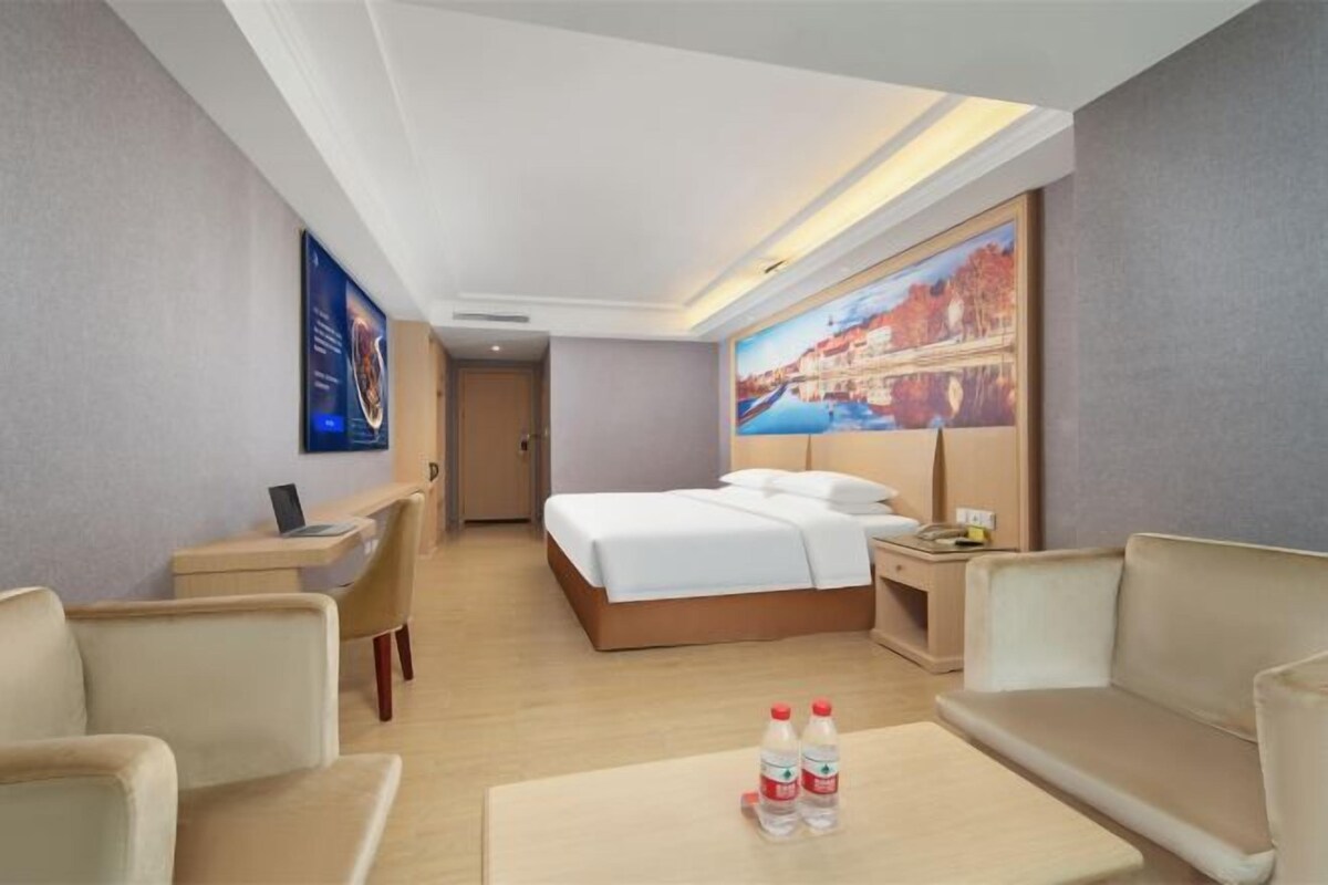 Ein Hotelzimmer mit Bett, Schreibtisch, Sessel, Sofa und einem Couchtisch mit zwei Flaschen.