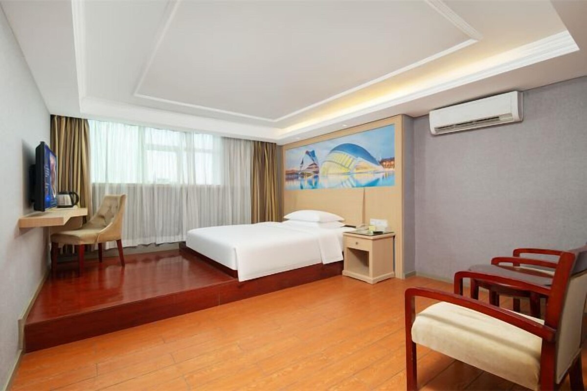 A hotel room with a bed, a desk, a chair, and a painting on the wall.