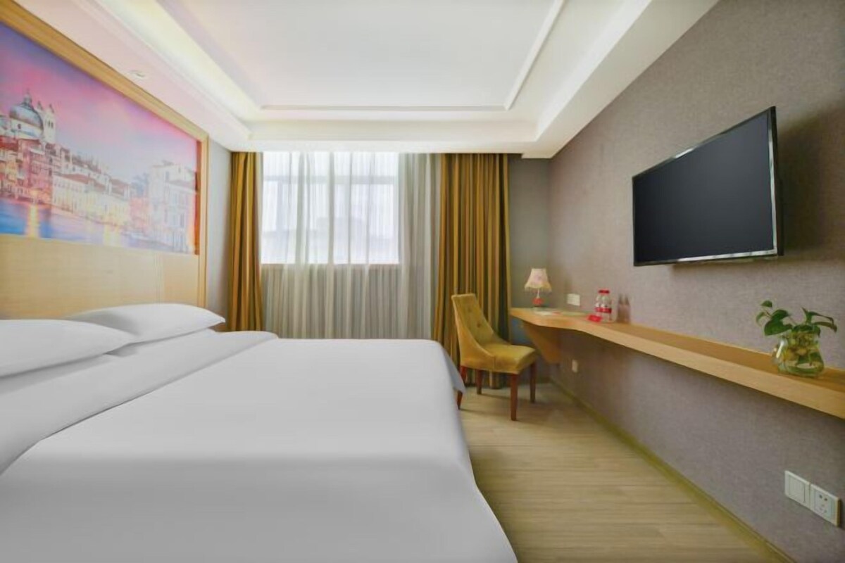 A hotel room with a bed, a desk, a chair, a television, and a painting on the wall.