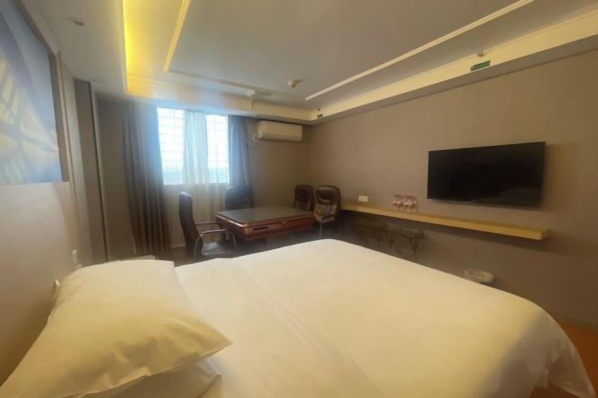 A hotel room with a large bed, a desk with a chair, a flat-screen TV mounted on the wall, and an air conditioning unit.