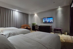 Ein Hotelzimmer mit zwei Betten, einem Fernseher, einem Schreibtisch und einem Sessel.