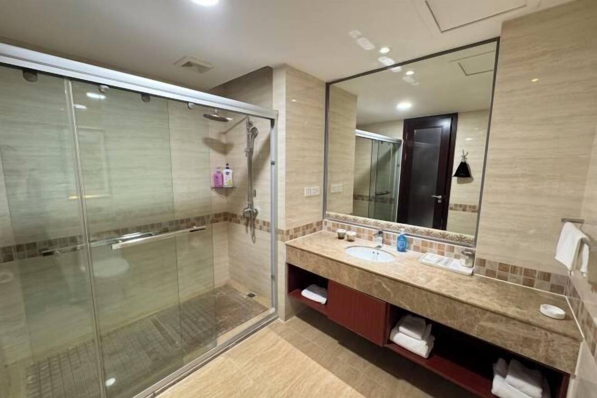 Une salle de bain moderne dotée d’une douche à parois de verre, d’un grand miroir et d’un meuble-lavabo avec un espace pour ranger les serviettes.