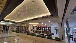 A spacious lobby with a high ceiling, a restaurant area, and a seating area with plants.