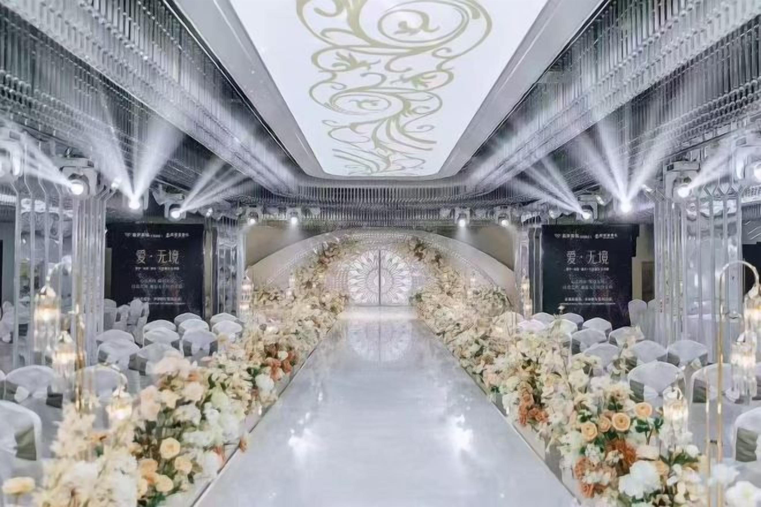 A long, narrow corridor with a reflective floor, flanked by white floral arrangements and clear glass partitions.