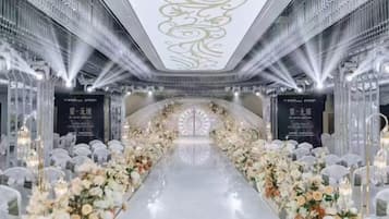 A long, narrow corridor with a reflective floor, flanked by white floral arrangements and clear glass partitions.