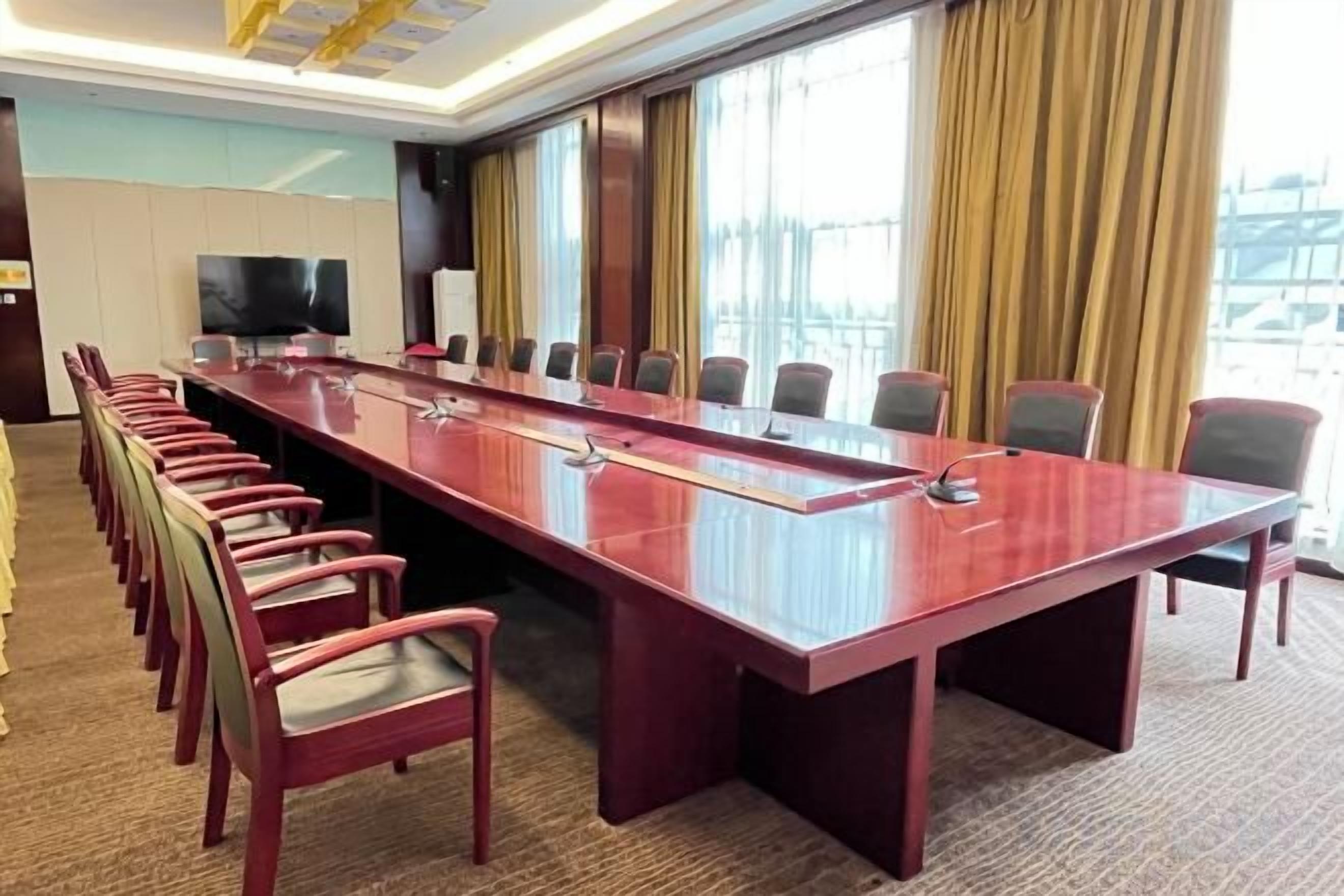 A conference room with a long table, chairs, a television, and a window with curtains.