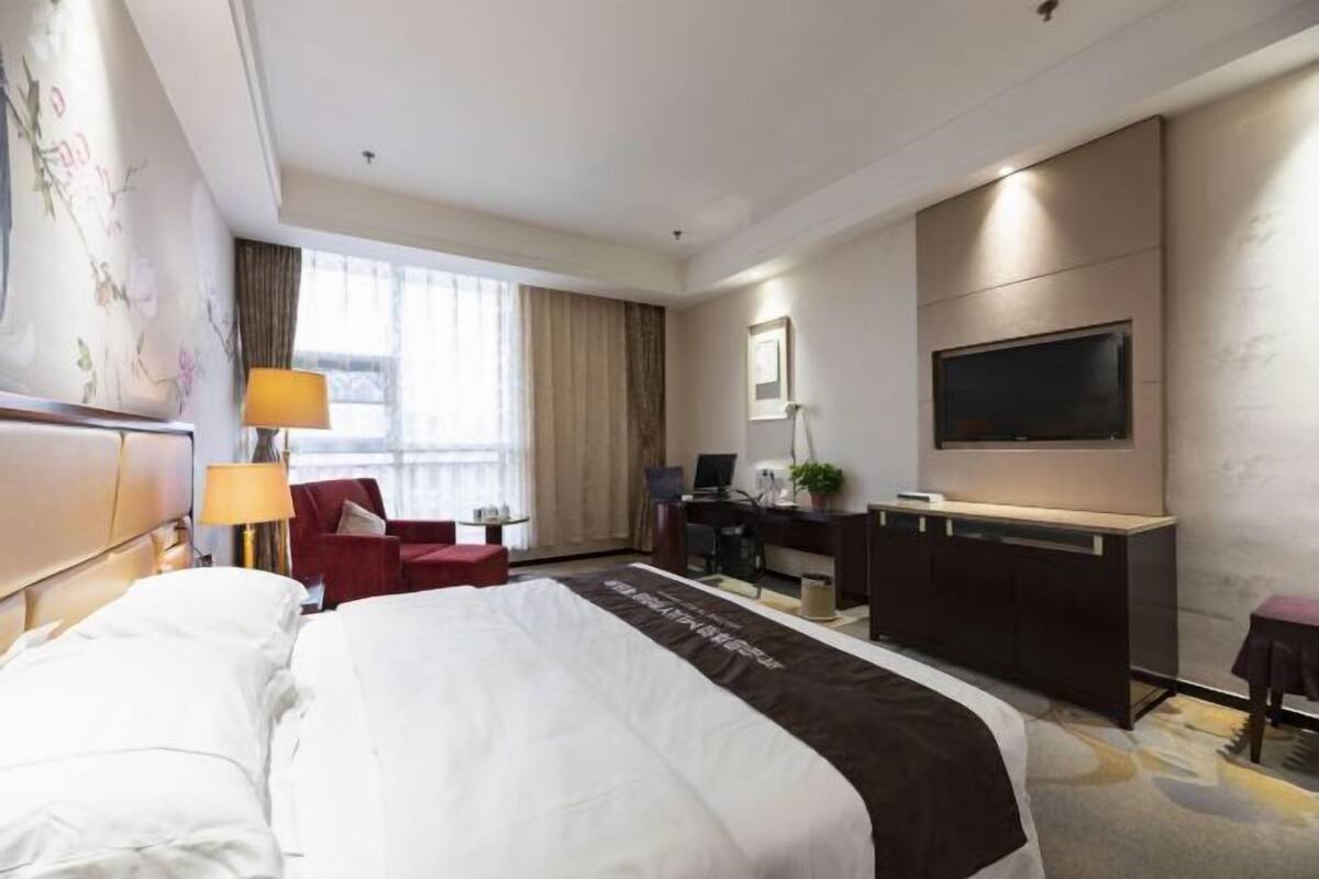 A hotel room with a large bed, a desk, a chair, a TV, and a window with curtains.