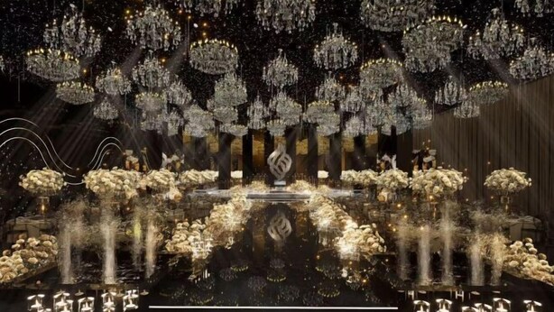 A grand hall with multiple chandeliers, a central stage, and rows of seating.