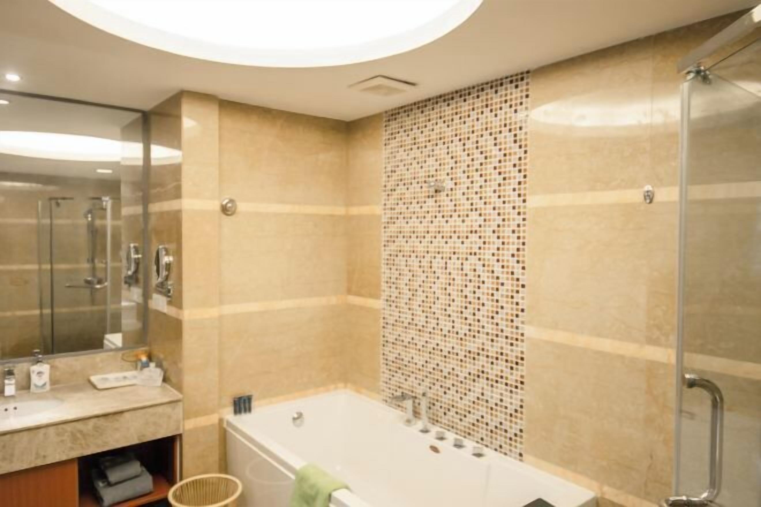 Une salle de bain avec une baignoire, un espace de douche vitré, un miroir et un mur carrelé.