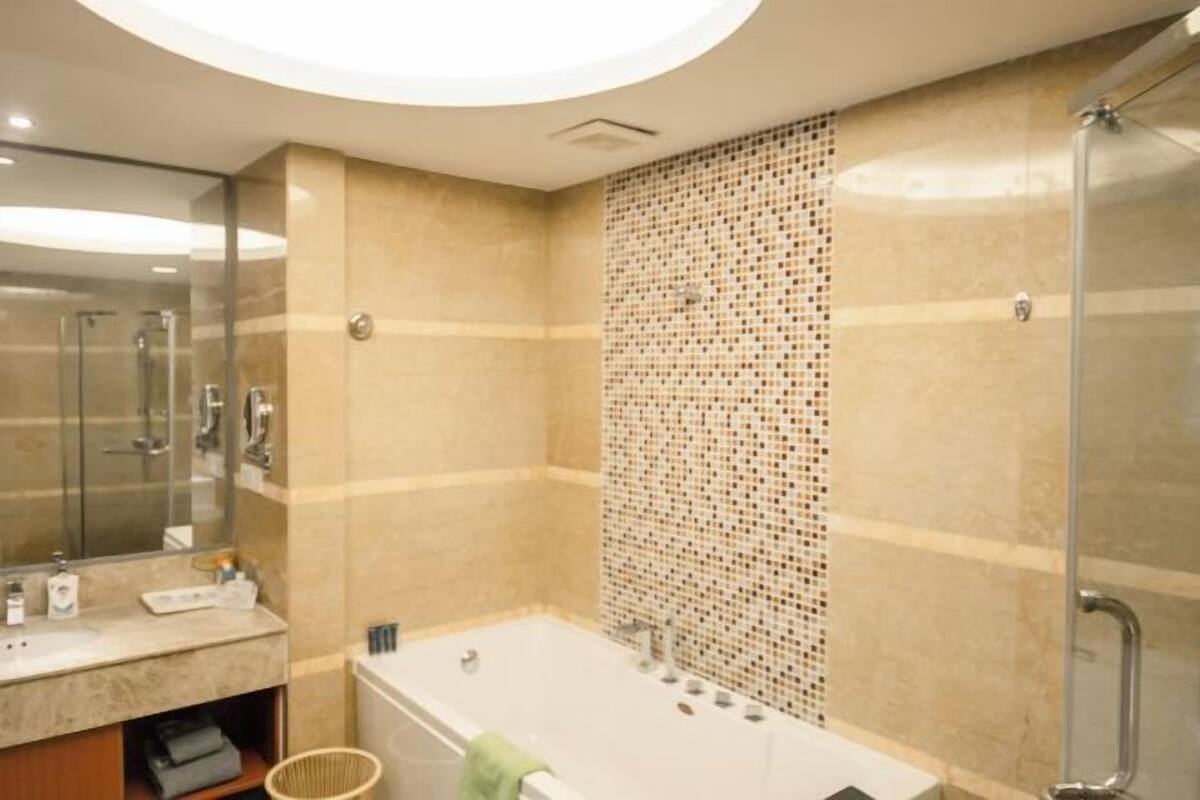 Une salle de bain avec une baignoire, un espace de douche vitré, un miroir et un mur carrelé.