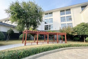 A building with a red pergola in the courtyard, surrounded by greenery and a paved walkway. - Linyi Hotel (Development Zone) (Linyi)