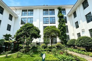 A building with multiple windows and a well-maintained garden with various plants and trees.