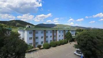 A multi-story hotel with a parking lot and a mountainous backdrop.