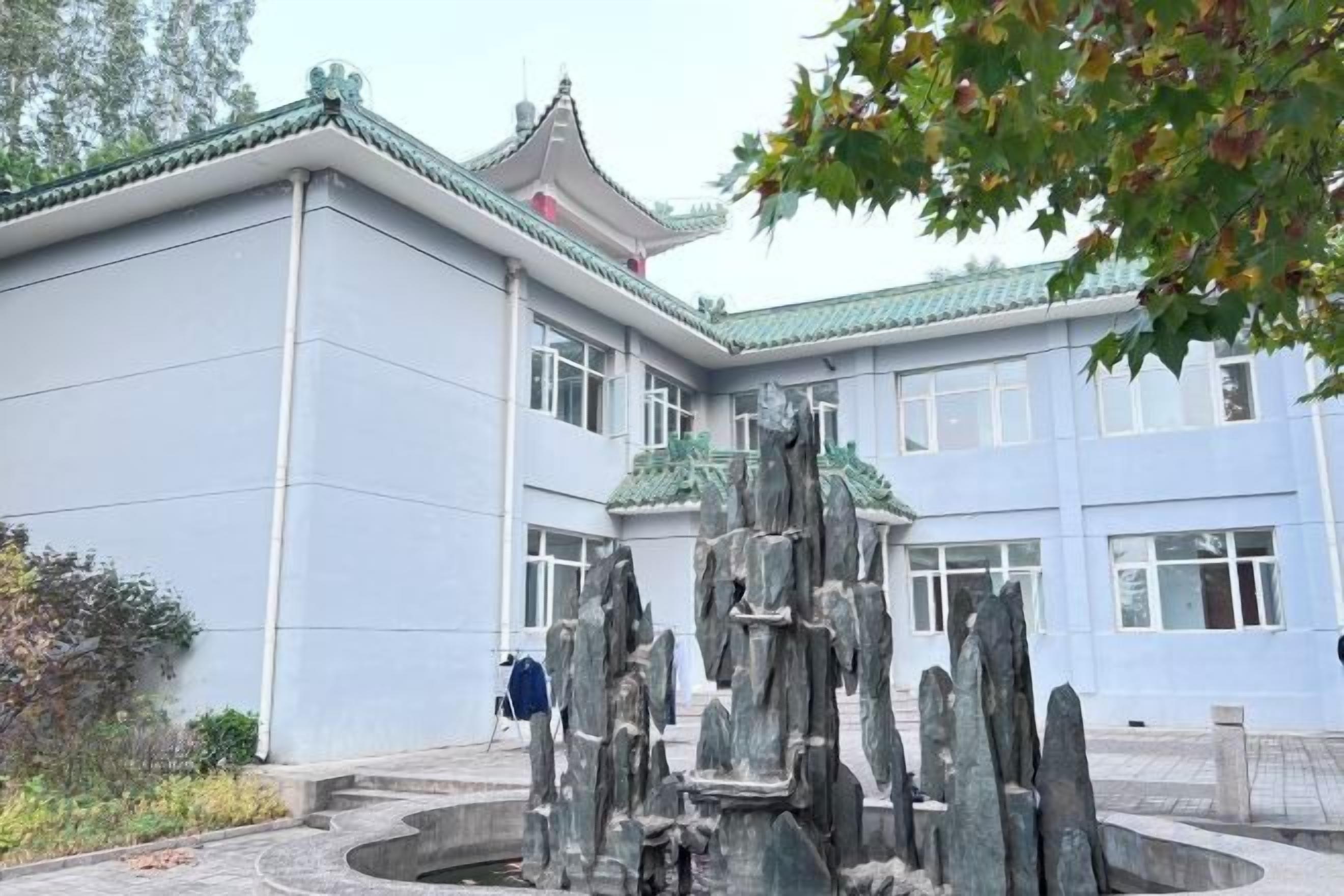A building with a traditional architectural style, a stone fountain, and a person walking in the foreground.