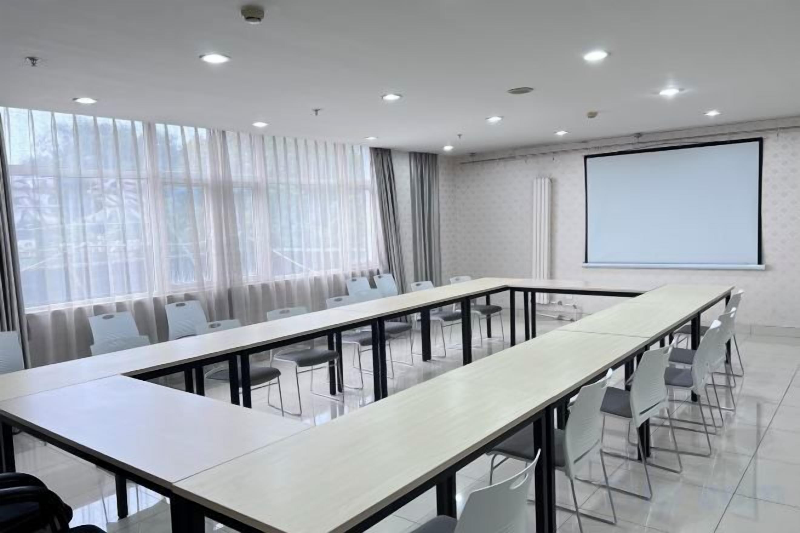 A conference room with a long table, chairs, a projector screen, and a large window with curtains.