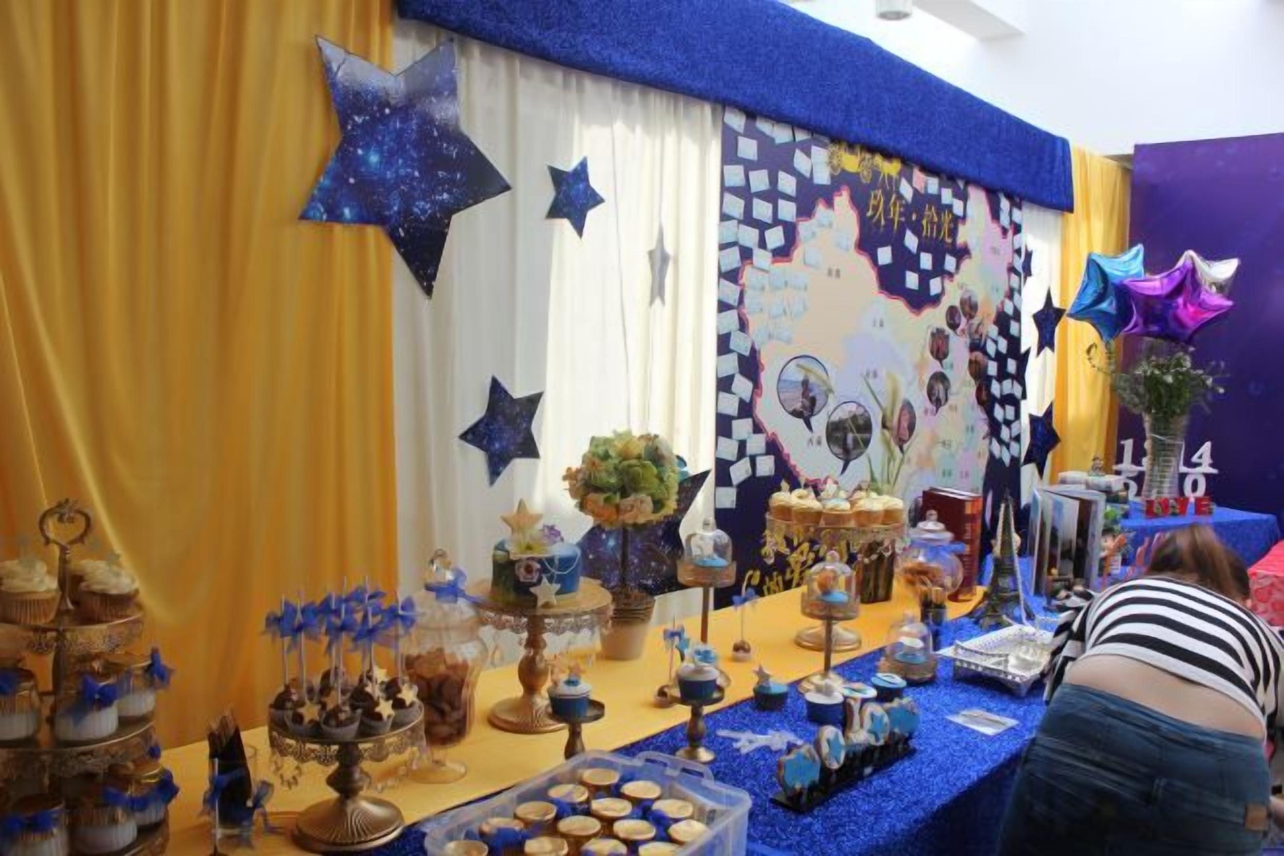 Un espacio decorado para un evento con un fondo temático de estrellas, una mesa con diferentes tipos de comida y una persona en primer plano.