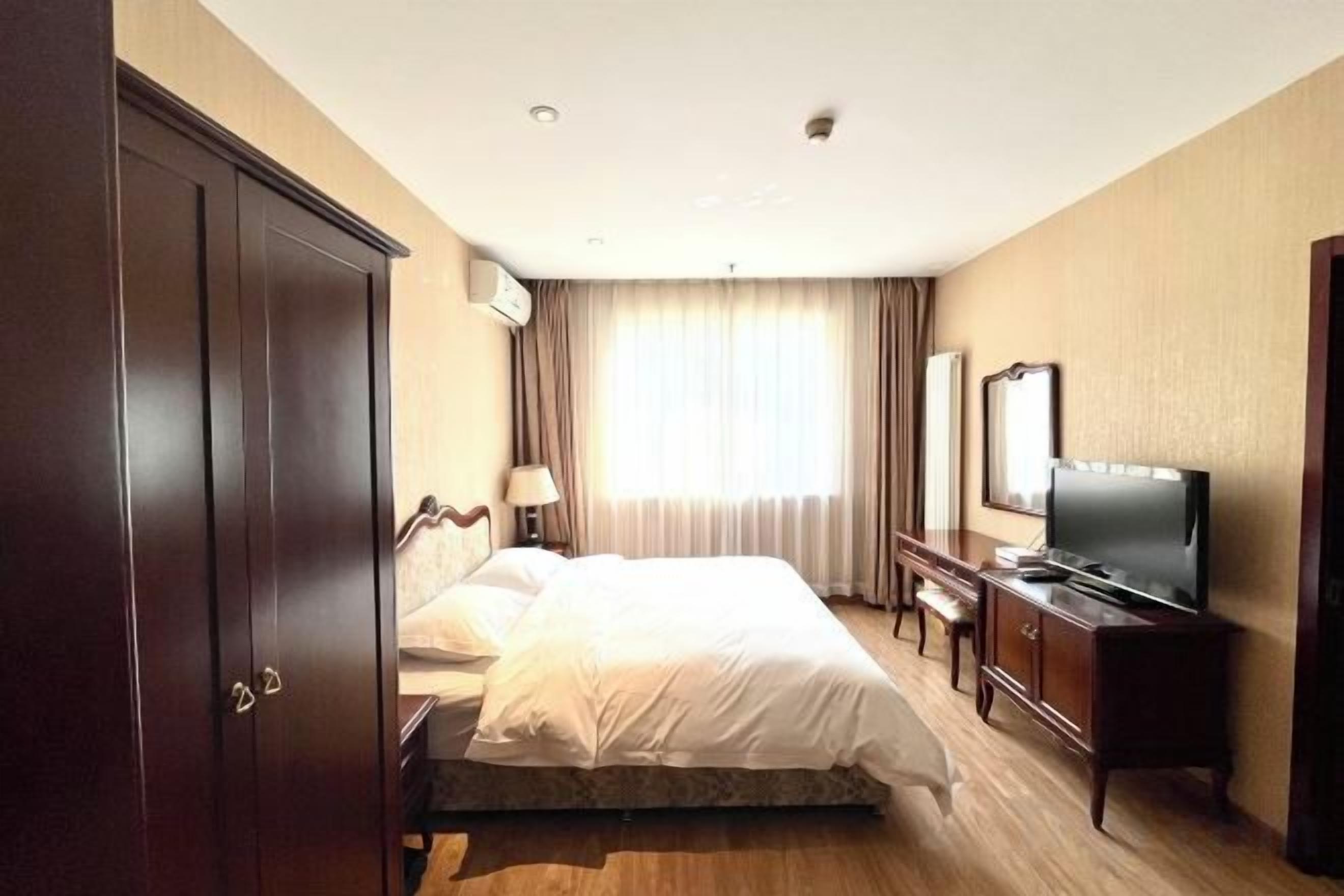 A hotel room with a bed, a TV, a wardrobe, and a desk.