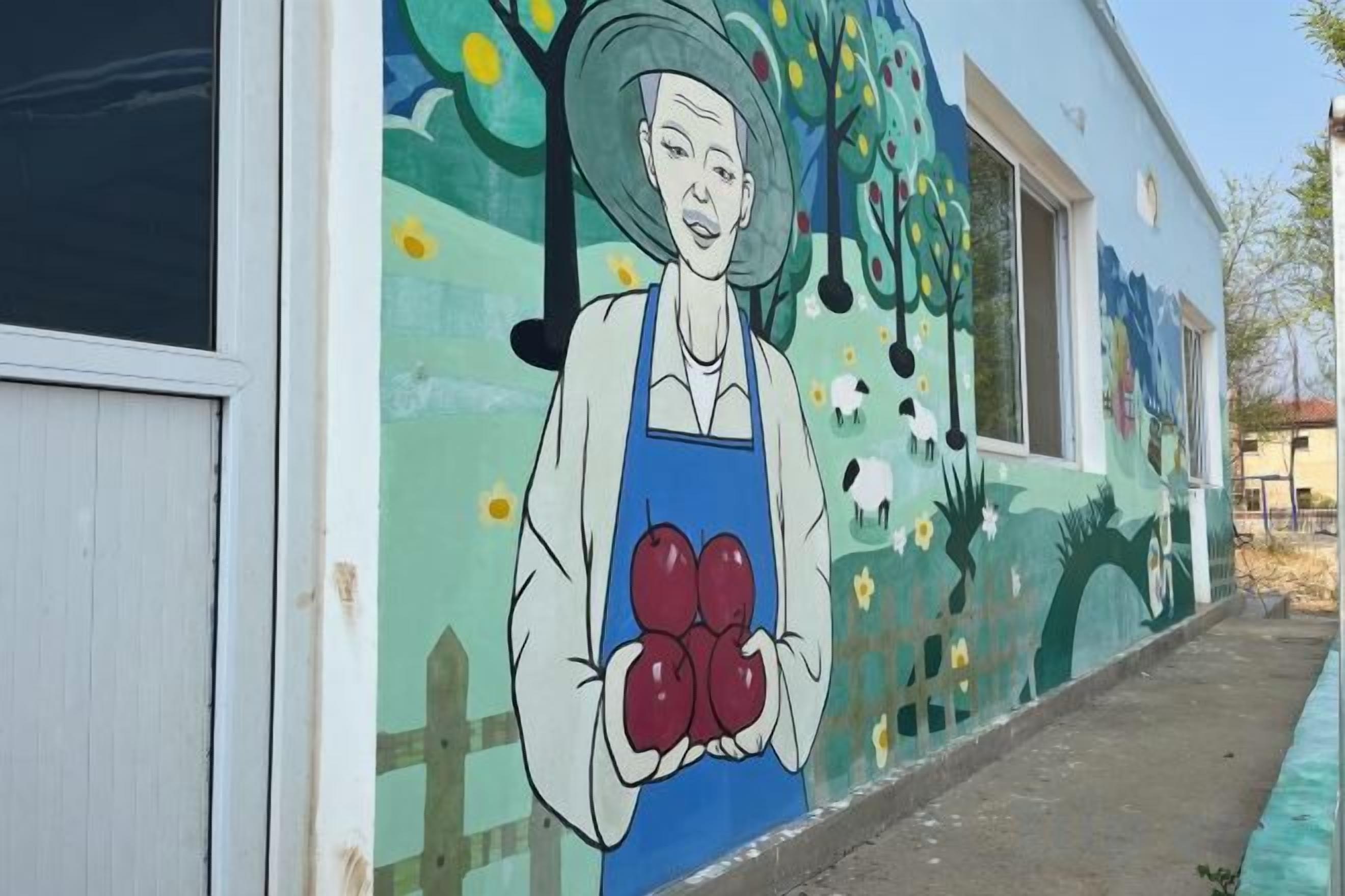 A mural on a building's exterior featuring a person holding apples.