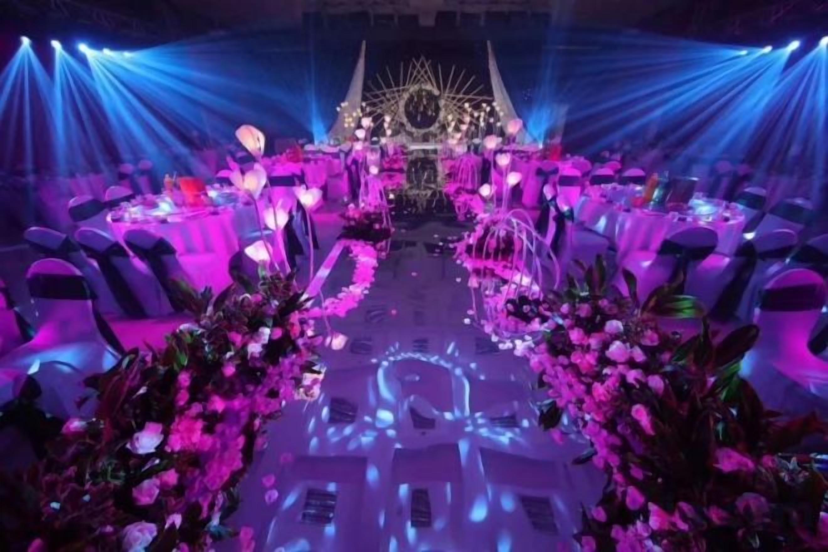 A banquet hall with tables arranged in a semi-circular fashion, centered around a stage with a decorative backdrop.