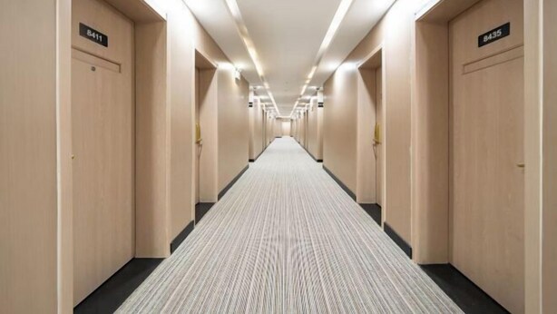 Un corridoio di un hotel con diverse porte, ognuna contrassegnata da un numero, e un pavimento rivestito di moquette.