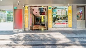 Ingresso di un hotel con facciata in vetro, segnaletica e pavimento piastrellato.