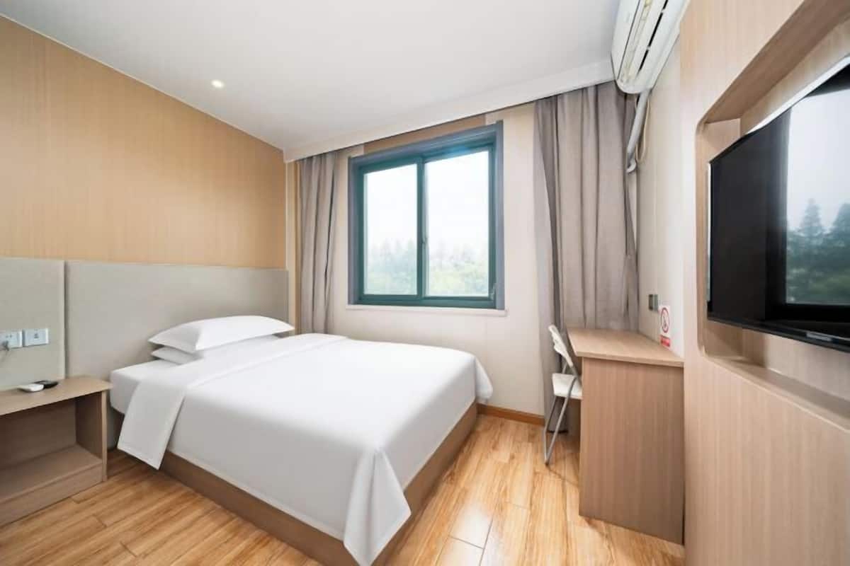 A hotel room with a bed, a desk, a TV, and a window with curtains.