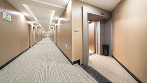 Un corridoio d'albergo con pavimento rivestito di moquette, porte su entrambi i lati e un cestino.