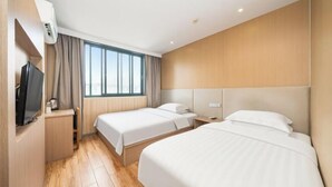 Camera d'albergo con due letti, televisione, una finestra con tende e una parete in legno.