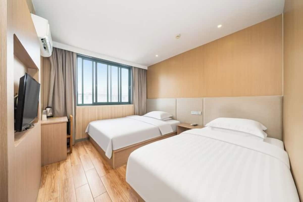 A hotel room with two beds, a TV, a window with curtains, and a wooden wall.