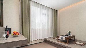 Una habitación de hotel moderna con un escritorio de madera, un cuenco de fruta, una botella de vino y una mesita con una planta.