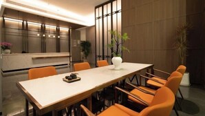 Un comedor moderno con una mesa larga y sillas naranjas, un jarrón blanco con plantas y una pared de madera con una ventana.