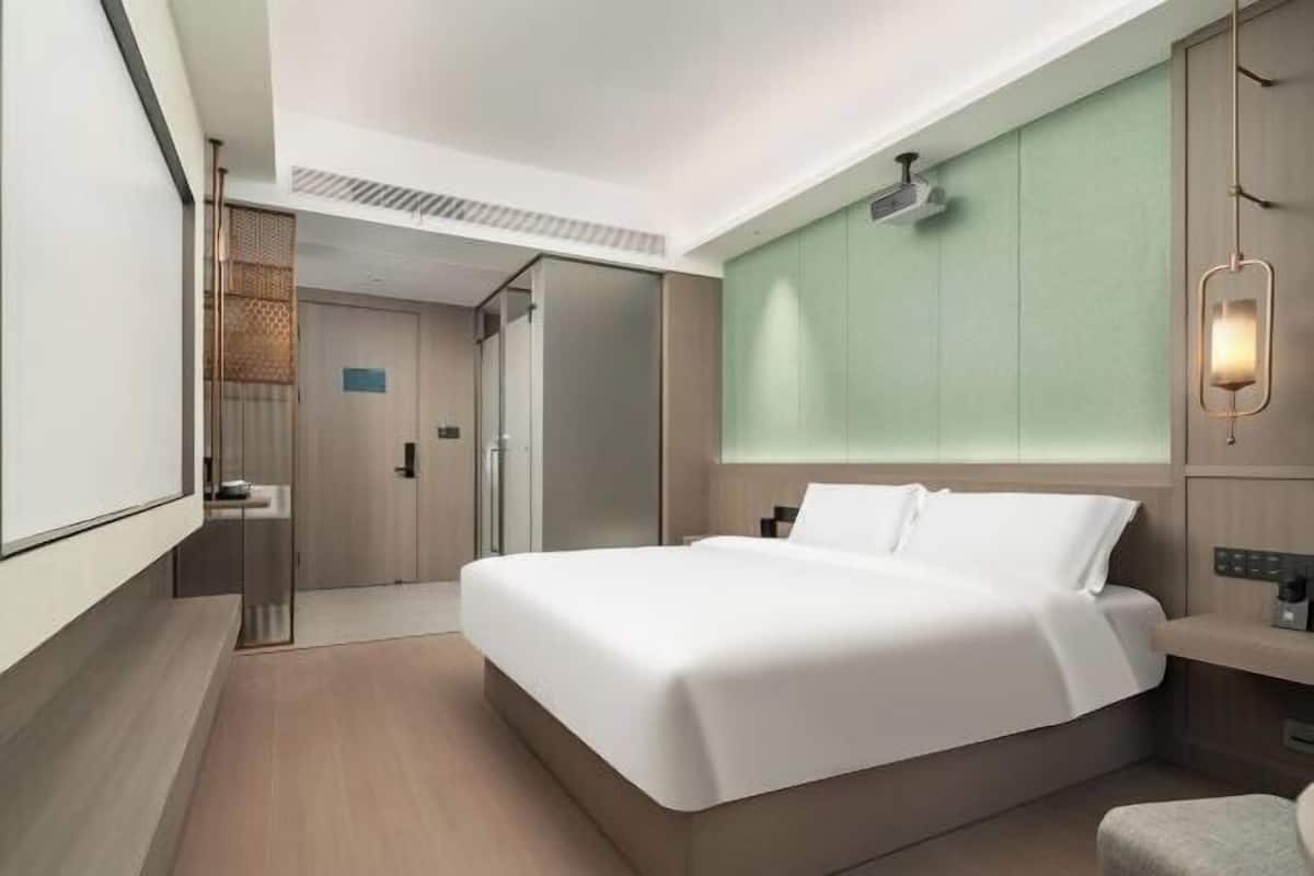 A modern hotel room with a large bed, a desk, and a shower area.