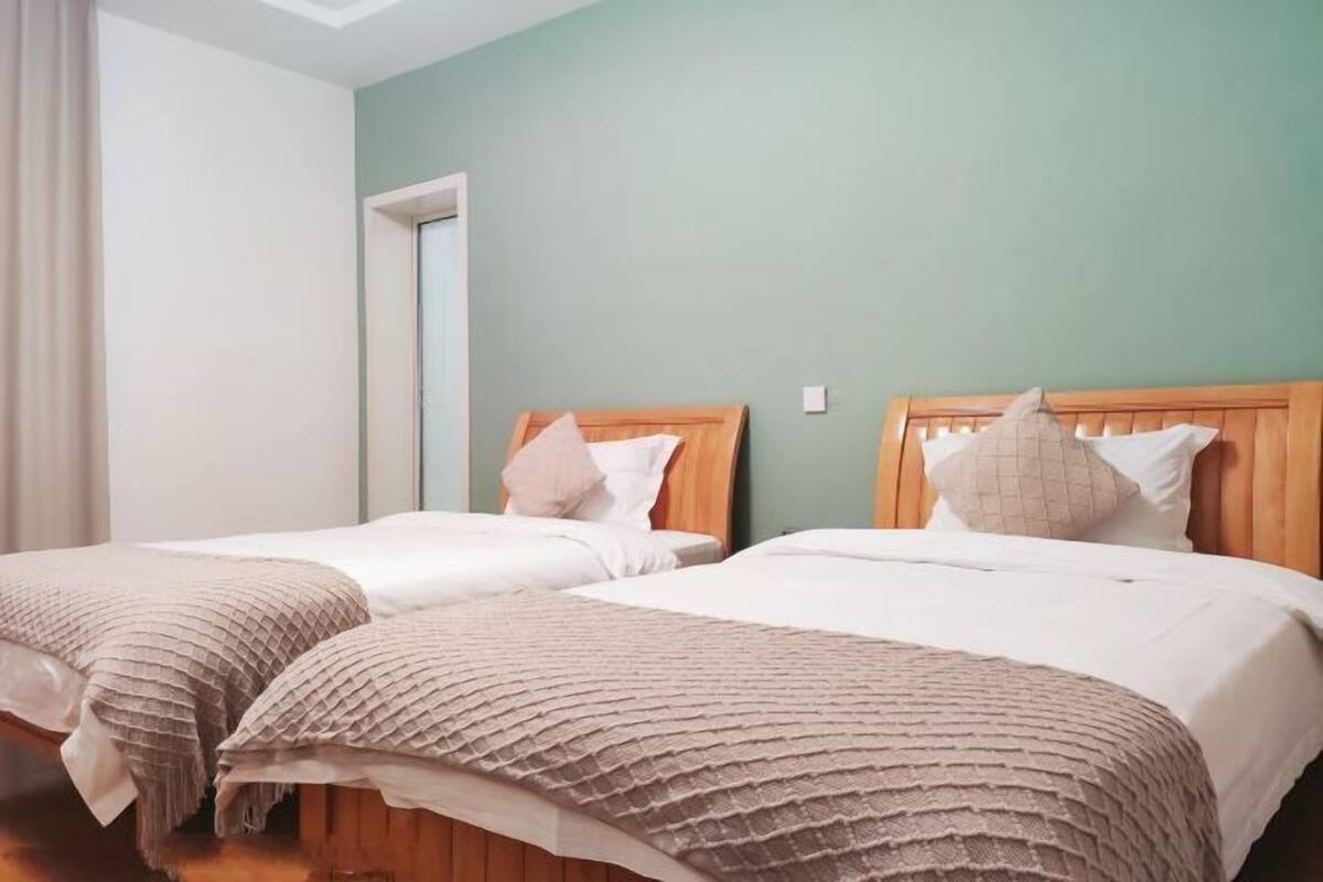 Ein Doppelzimmer mit zwei Betten, Holz-Kopfteilen und einer hellgrünen Wand.