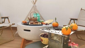 Un espace intérieur chaleureux et accueillant, avec une table ronde dressée pour un repas, une petite tente et un présentoir en métal décoratif orné d’oranges.