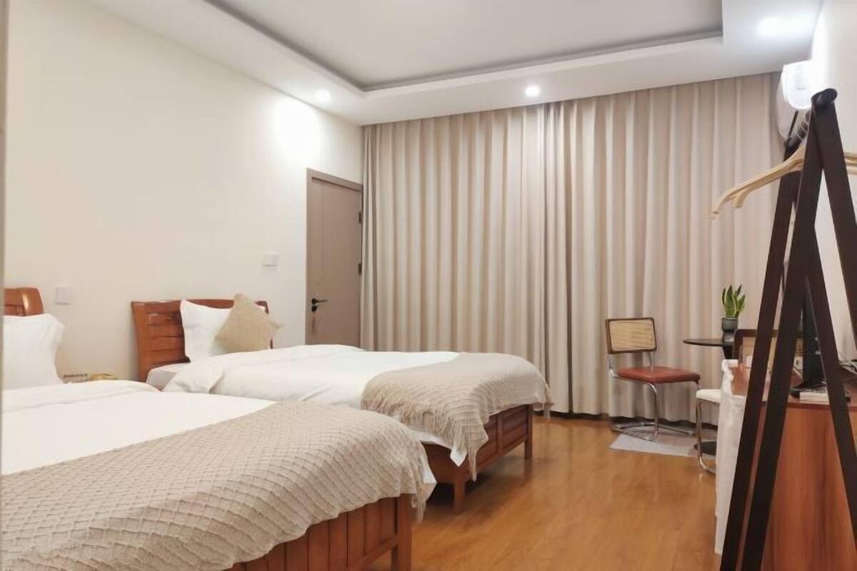 Ein Hotelzimmer mit zwei Betten, einem Schreibtisch, einem Stuhl und einem großen Fenster mit Vorhängen.