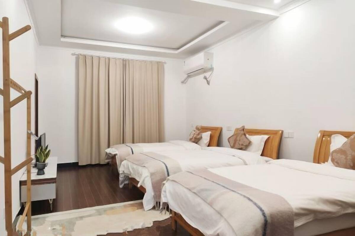 Ein Hotelzimmer mit zwei Betten, einem Schreibtisch, einer Pflanze und einem Fenster mit Vorhängen.