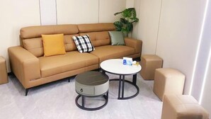 Un salon moderne avec un canapé marron, deux poufs ronds, une table basse blanche et une plante en pot.