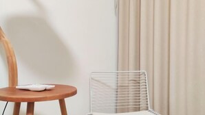 Une pièce avec une chaise en bois, un radiateur blanc et un rideau beige.
