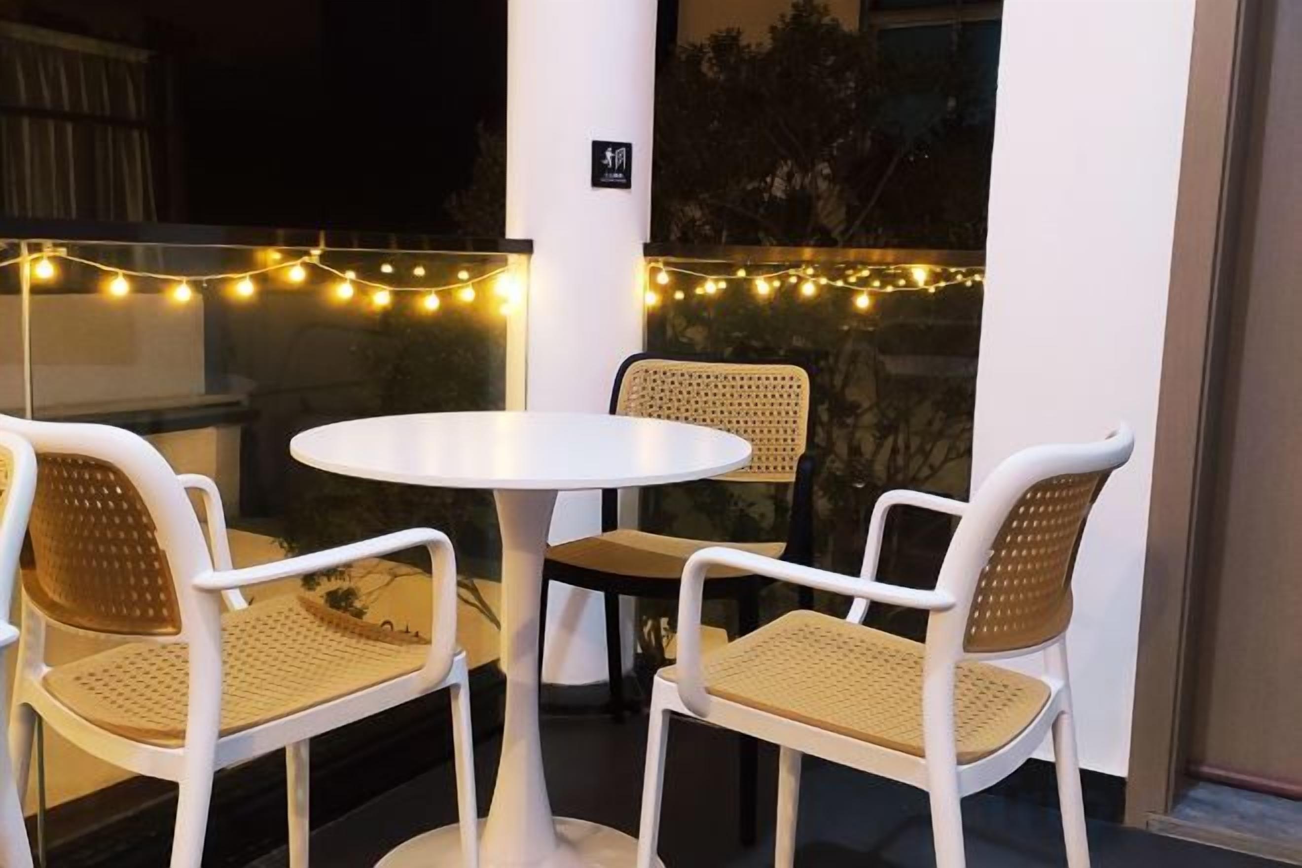 An outdoor seating area with a round table and four chairs, string lights, and a view of the cityscape.