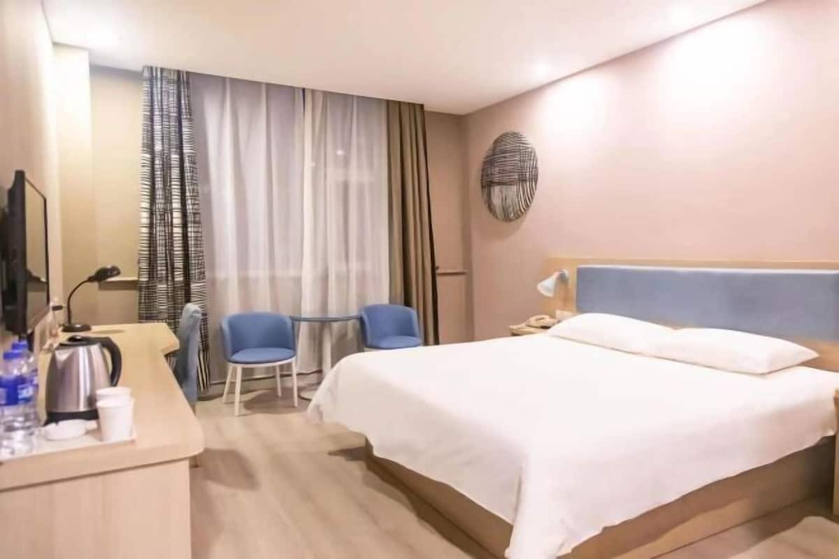 Une chambre d’hôtel avec un lit, un bureau doté d’une bouilloire, des chaises et une fenêtre avec des rideaux.