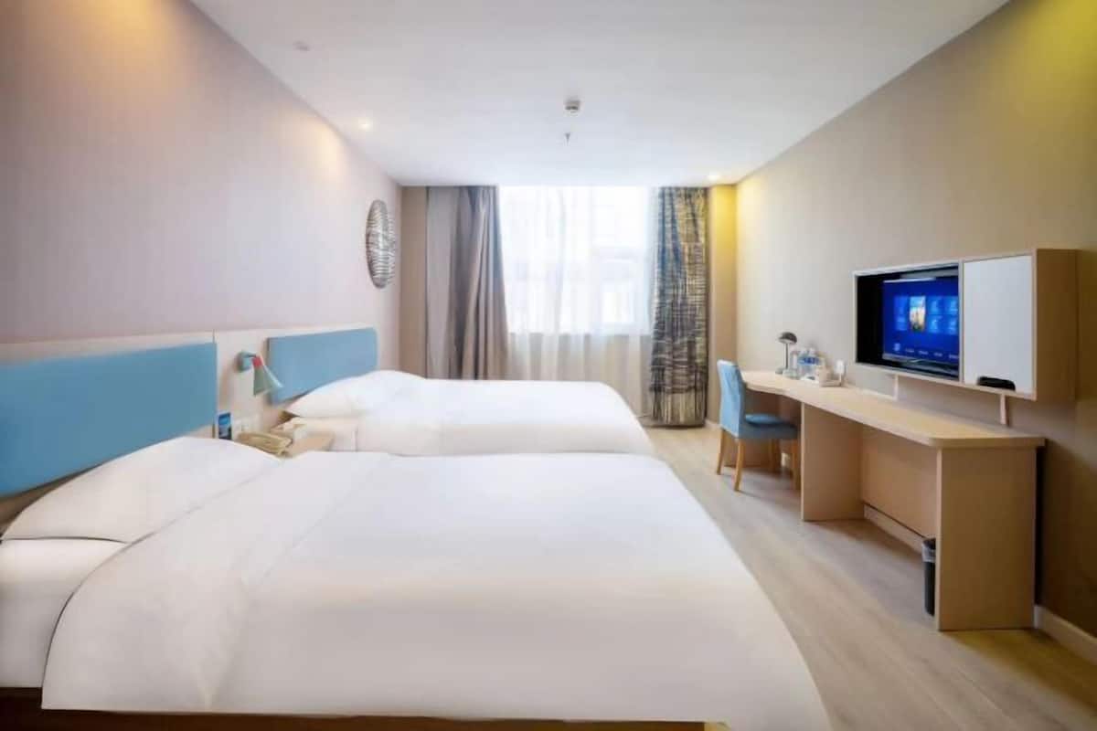 Une chambre d’hôtel avec deux lits, un bureau, une télévision et une fenêtre avec des rideaux.